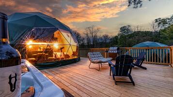 A wooden deck with a tent, outdoor furniture, and a grill.