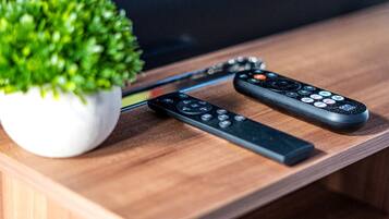 Two remote controls on a wooden surface with a potted plant beside them.