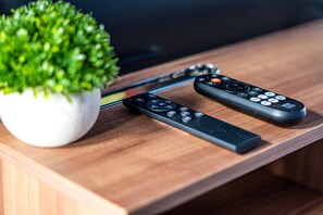 Two remote controls on a wooden surface with a potted plant beside them.