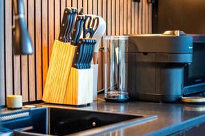 A kitchen counter with a coffee machine, a knife block, and a glass.