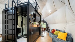 Un intérieur moderne et compact, doté d’une kitchenette, d’un coin salon agrémenté de coussins colorés et d’une grande structure en forme de dôme aux motifs géométriques.
