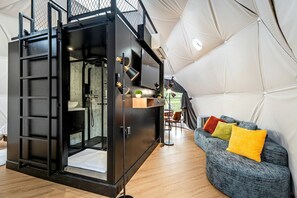 Ein kompakter, moderner Innenraum mit Küchenzeile, einer Sitzecke mit bunten Kissen und einer großen, geometrischen Kuppel.