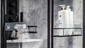Une salle de bain avec une douche à parois de verre, un porte-serviettes noir et des flacons d’après-shampoing hydratant Dove disposés sur une étagère.