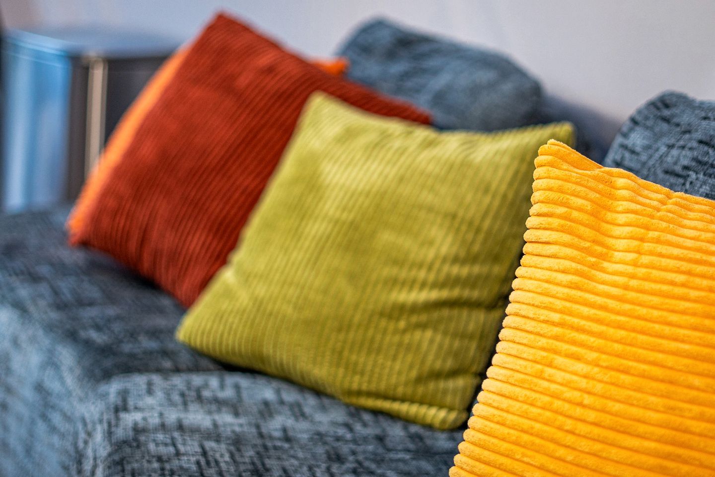 A bed with a grey blanket and three pillows in red, green, and yellow.
