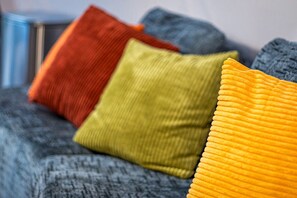 A bed with a grey blanket and three pillows in red, green, and yellow.