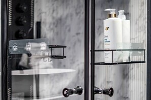 A bathroom with a glass shower enclosure, a black towel rack, and Dove daily moisture conditioner bottles on a shelf.