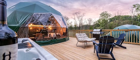 A tented outdoor area with a hot tub, deck chairs, and a grill.