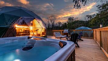 A hot tub on a wooden deck, a tent with a telescope, and a grill.