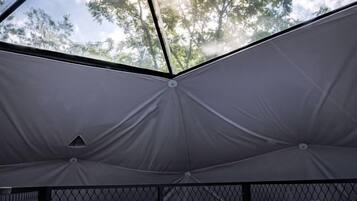 Tenda com cama interna, janela de tela e vista para árvores.