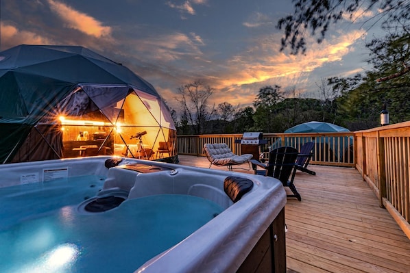A hot tub on a wooden deck, a tent with a telescope, and a grill.