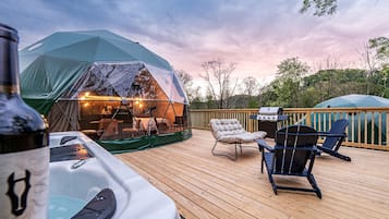 A tented outdoor area with a hot tub, deck chairs, and a grill.