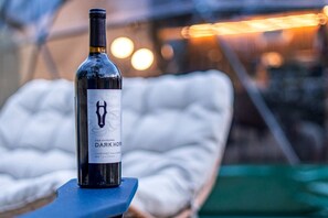 A bottle of wine on a table with a white cushioned chair in the background. - Geodesic Dome Retreat with Hot Tub & Fire Pit in Bluefield, West Virginia (Blueflield)