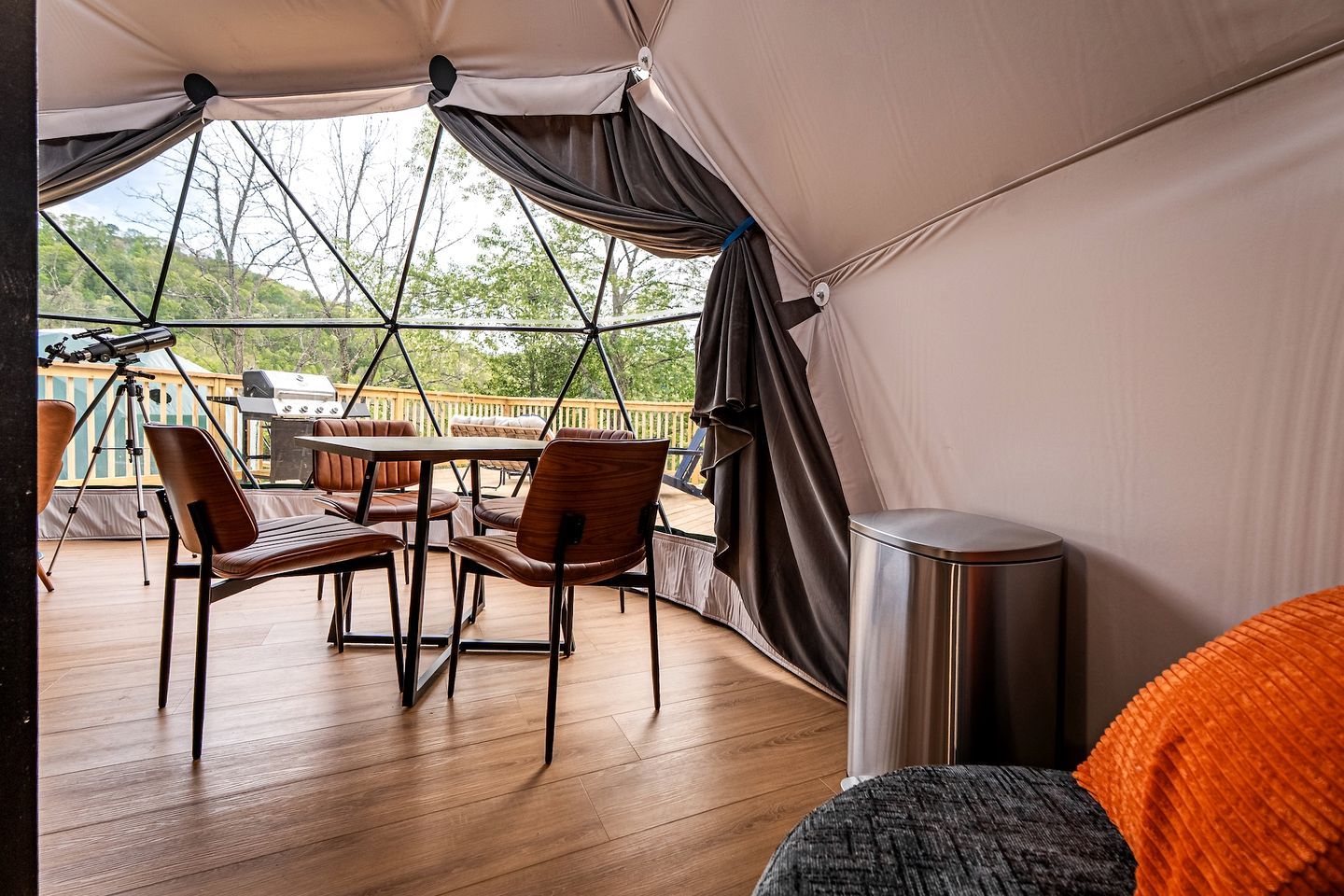 A tented outdoor area with a table and chairs, a grill, and a telescope.
