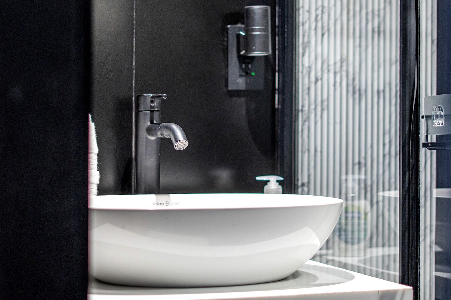 Un baño moderno con un lavamanos blanco, un grifo negro y un dispensador de jabón.