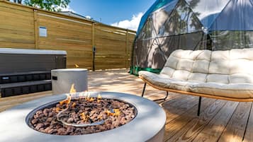 A fire pit with burning wood, a cushioned outdoor chair, and a covered area, all on a wooden deck.