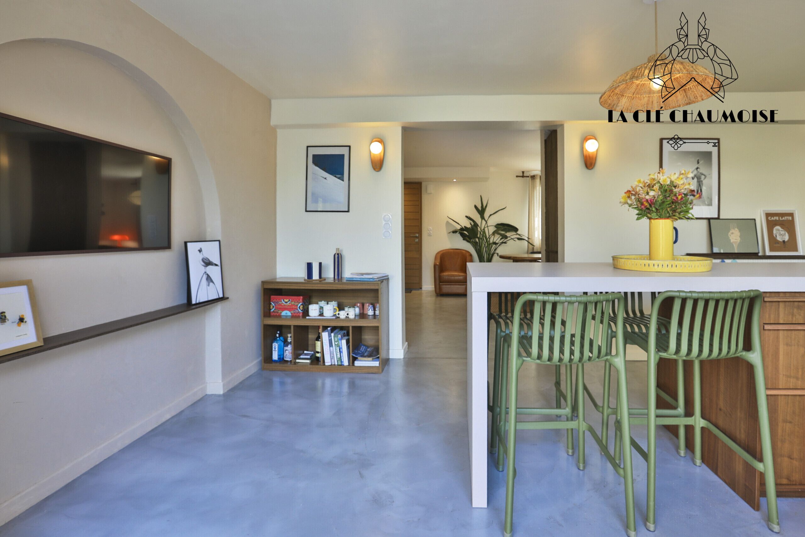 Una cucina moderna con un'area bar, un tavolo da pranzo e sedie. Si nota una libreria con libri e oggetti decorativi, una pianta in vaso e un quadro appeso al muro.