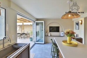 A modern kitchen with a built-in sink, a dining area with chairs, a large window, and a ceiling fan. - La Dolce Vita • Maison de charme 6 pers à La Chaume (Les Sables-d´Olonne)