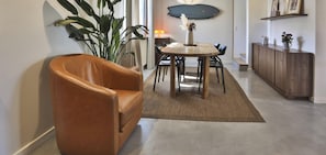 Ein Essbereich mit einem Holztisch und Stühlen, einem braunen Ledersessel, einer großen Pflanze und einem Holzschrank mit Dekorationen.