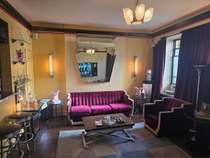 Une pièce comprenant un canapé, une table basse, un coin bar avec des tabourets, un miroir et un lustre.