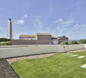 A modern building with a sign reading 'LA VIGIE VACANCES' and a wind turbine in the background. - La Villa du Phare — Vue océan • 10 pers (Les Sables-d´Olonne)