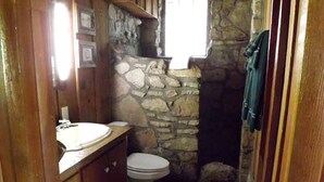Un baño pequeño con pared de piedra, tocador de madera, inodoro y ventana.