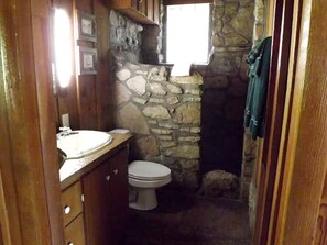 Ein kleines Badezimmer mit Steinwand, Holzwaschtisch, Toilette und Fenster.