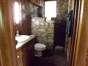 Ein kleines Badezimmer mit Steinwand, Holzwaschtisch, Toilette und Fenster.