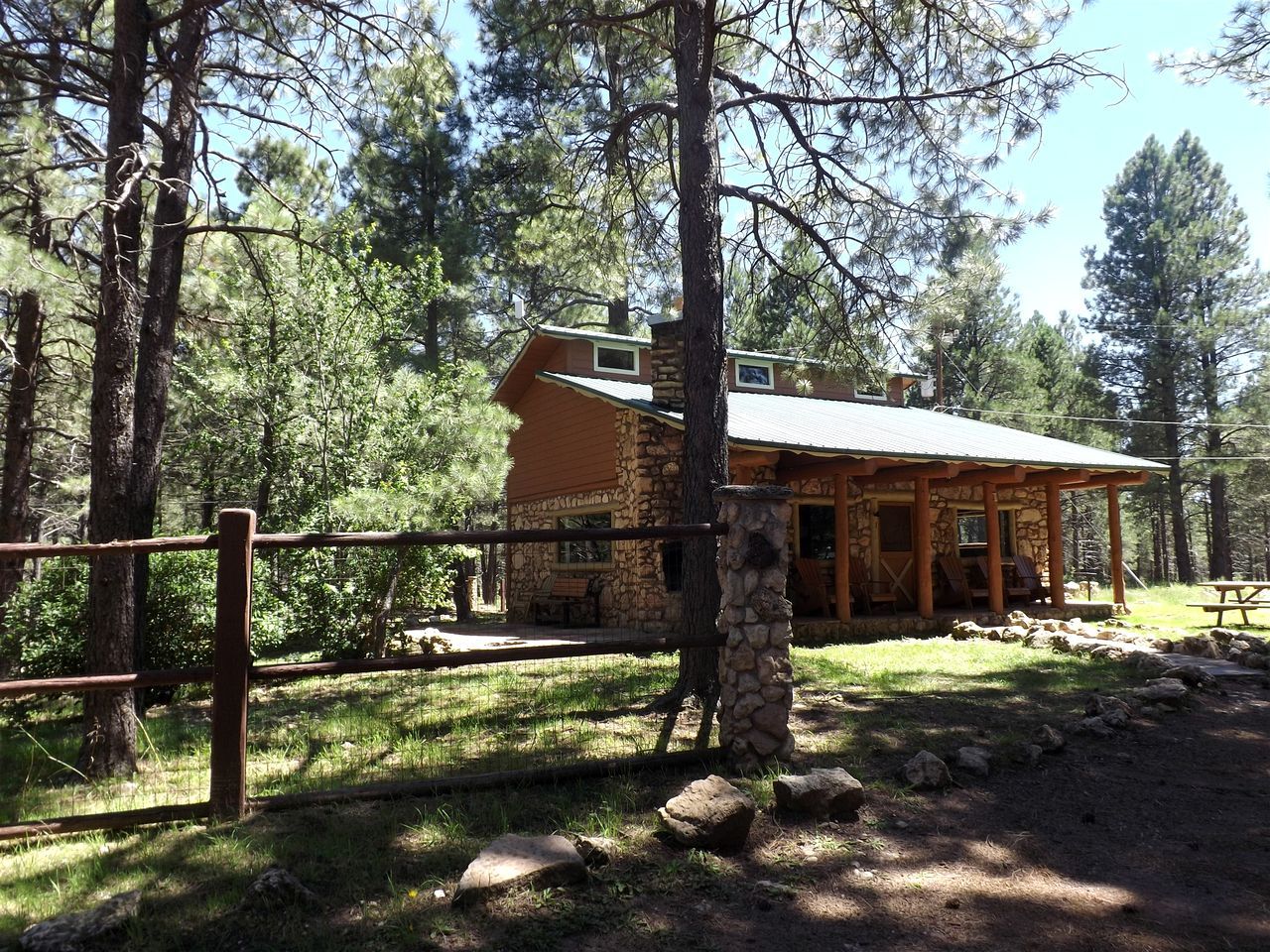 A rustic lodge with a stone exterior, a covered porch, and a fenced outdoor area.