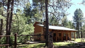 Un lodge rústico con fachada de piedra, un porche cubierto y un área exterior cercada.