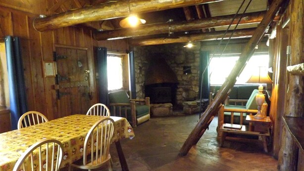 Un comedor rústico con chimenea de piedra, vigas de madera y una escalera que sube a un nivel superior.