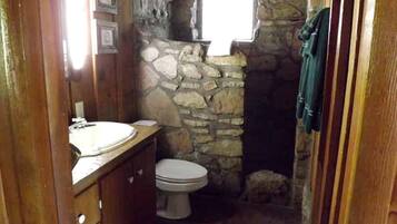 Une petite salle de bain avec un mur en pierre, un meuble-lavabo en bois, des toilettes et une fenêtre.