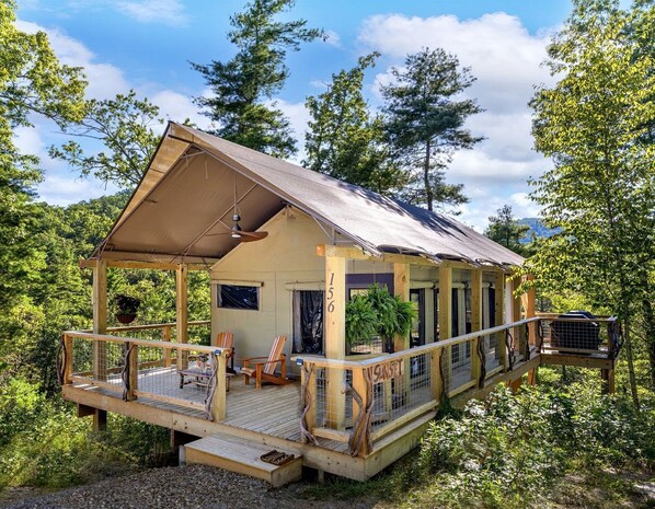 A wooden cabin with a covered porch, a small deck, and a sign reading '156'.