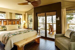 A bedroom with a bed, a bench, a chair, a wooden ceiling fan, and a sliding glass door leading to an outdoor deck.