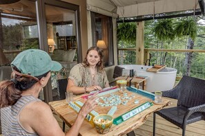 A wooden table with a Mahjong game set, a bowl of snacks, and a hot tub in the background.