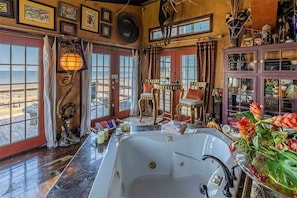 Een ruime badkamer met een groot bad, meerdere ramen en uitzicht op het strand.