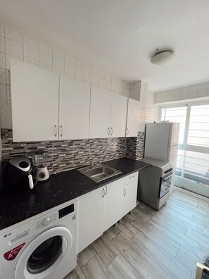 A modern kitchen with white cabinets, a black countertop, a built-in washing machine, and a refrigerator. - Charming 1-bedroom Apartment in the Heart of Madrid (Madrid)