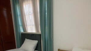 A room with two single beds, a wooden door, and teal curtains. - Charming 1-bedroom Apartment in the Heart of Madrid (Madrid)
