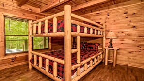 Ein Stockbett mit karierter Decke, ein kleiner Tisch mit Lampe und ein Fenster mit Rollläden.