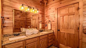 Ein Badezimmer im Holzblockhaus-Stil mit einer Arbeitsplatte aus Granit, einem Waschbecken und einem Spiegel.