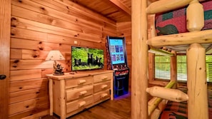 Ein Holzblockhaus-Interieur mit Fernseher, Spielkonsole und Etagenbett.