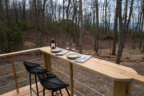 Eine Holzterrasse mit einem für zwei Personen gedecktem Tisch, einer Laterne und einem Stuhl.