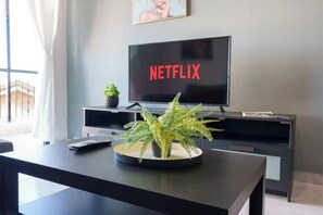 Un saló modern amb un televisor de pantalla plana que mostra 'NETFLIX', un clorofil·la en un gresol rodó i un sofà de color fosc.
