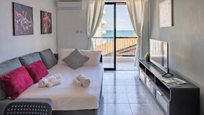 Habitació d'hotel moderna amb llit, televisió, escriptori i un balcó amb vista al mar.
