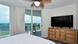 Een slaapkamer met een groot bed, een televisie, een houten dressoir en een balkon met uitzicht.