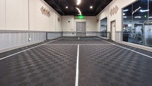 Ein geräumiger Innenbereich mit Schachbrettmuster-Boden, einem grünen Fluchtzeichen und Trainingsgeräten im Hintergrund.