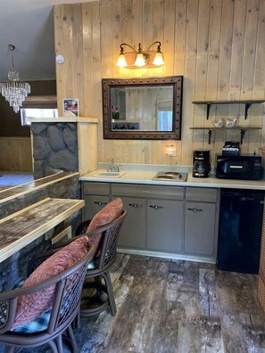 Une cuisine aux murs lambrissés en bois, avec un mur d’accent en pierre, un coin bar doté de chaises rembourrées, un four à micro-ondes encastré et un lustre.