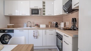 Una cocina moderna con armarios blancos, microondas integrado, cafetera y lavadora.