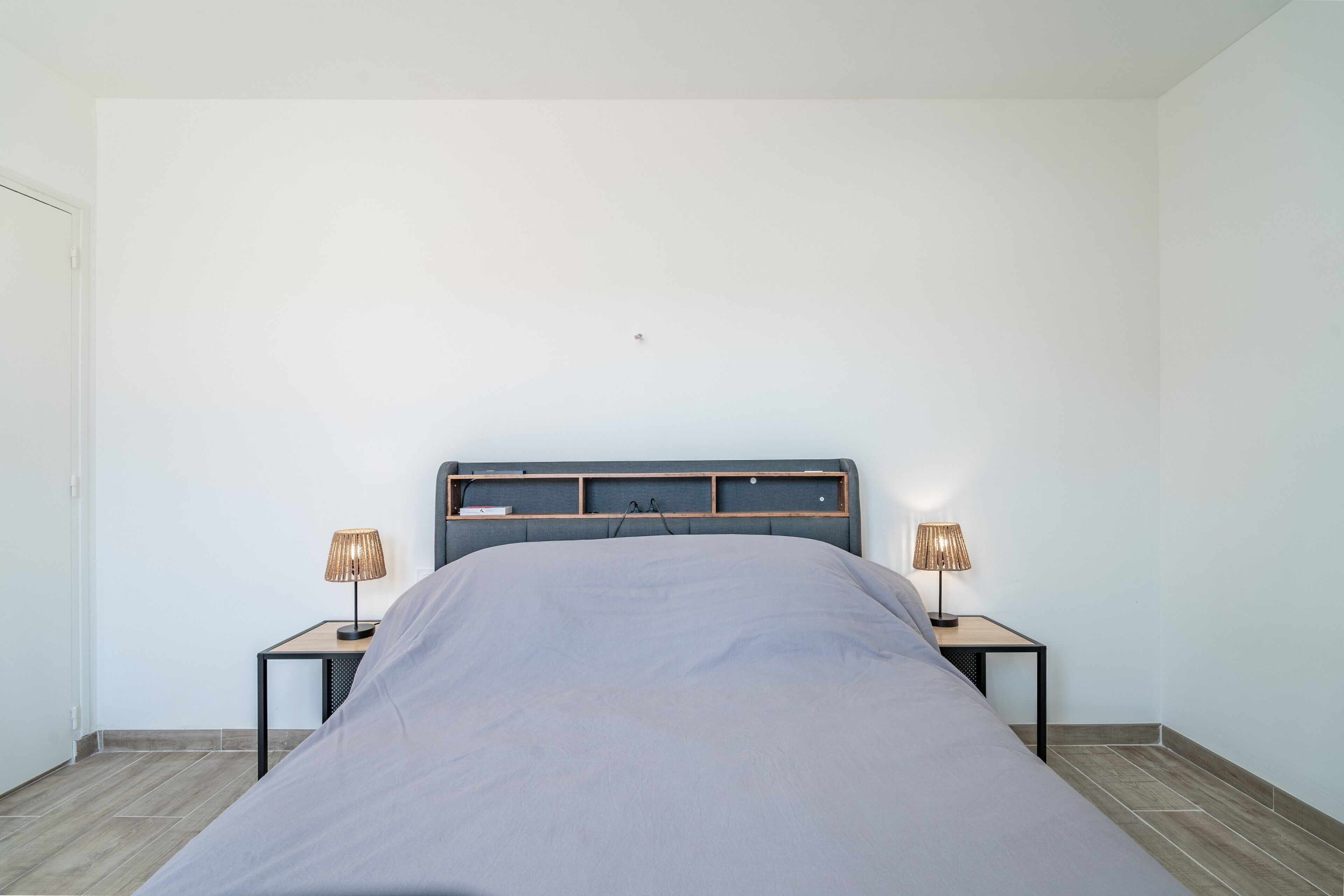 Une chambre à coucher avec un lit, deux tables de chevet avec des lampes et une tête de lit en bois.