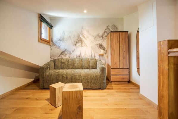 Ein Schlafzimmer mit Galeriemodus, Holzboden, einem grünen Sofa, einem Holzschrank und einer Bergwandmalerei.
