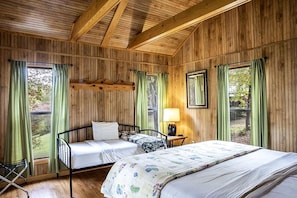 Una habitación con paneles de madera, dos camas, una mesita de noche y un ventanal con cortinas.
